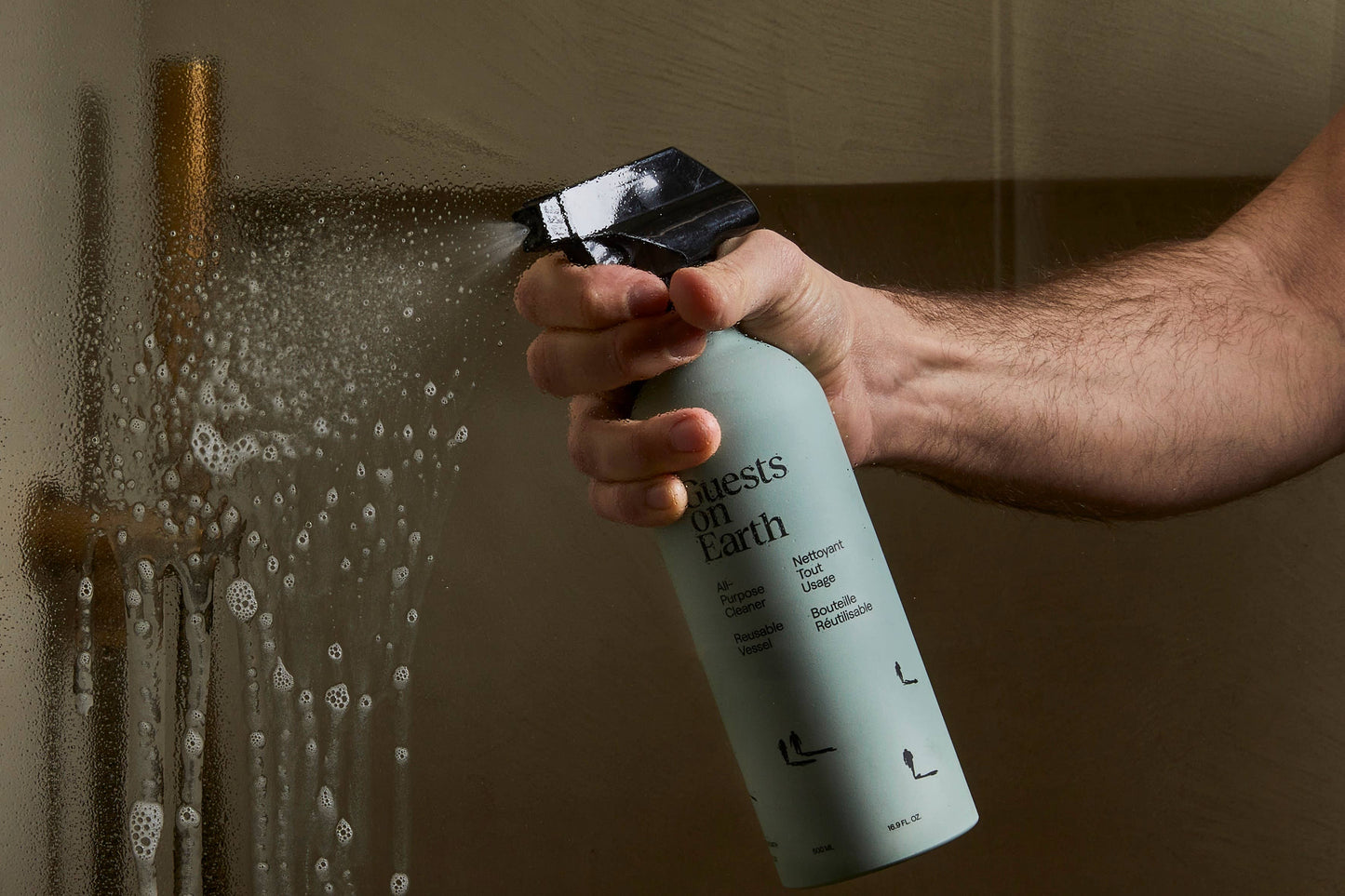 Person using Guests on Earth All-Purpose cleaner to clean a shower wall.