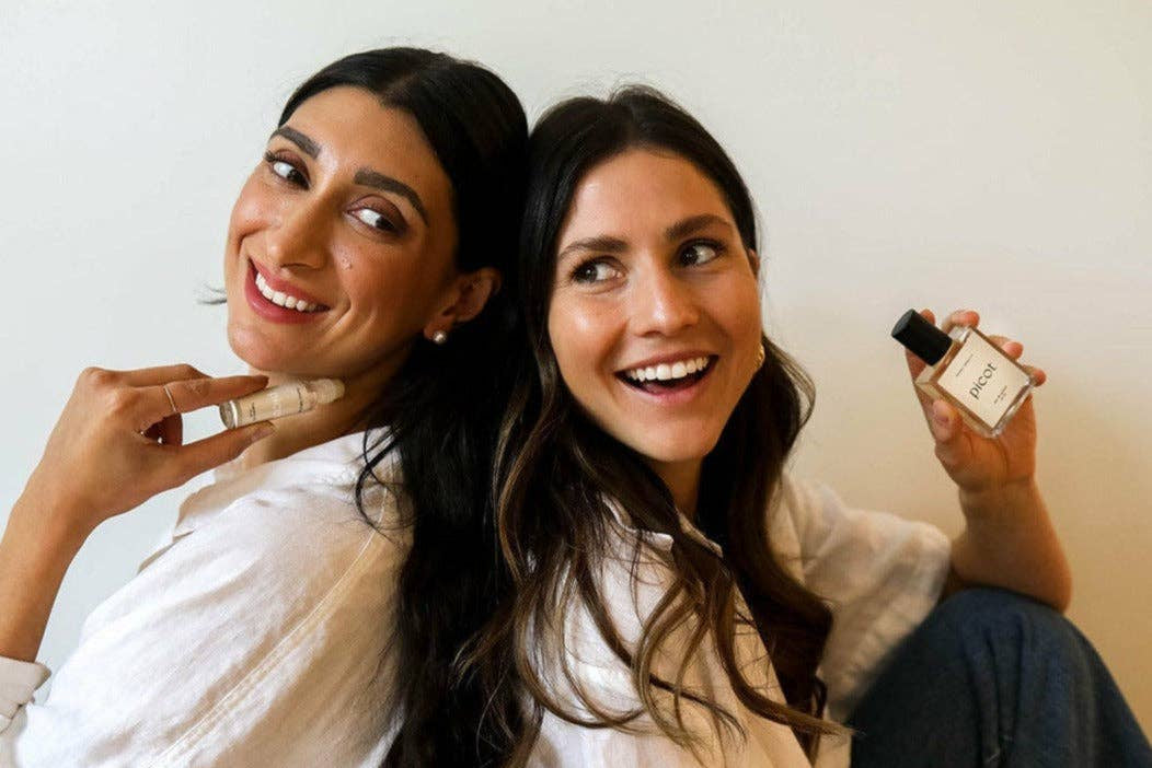 Two women holding Picot perfume products against a plain background