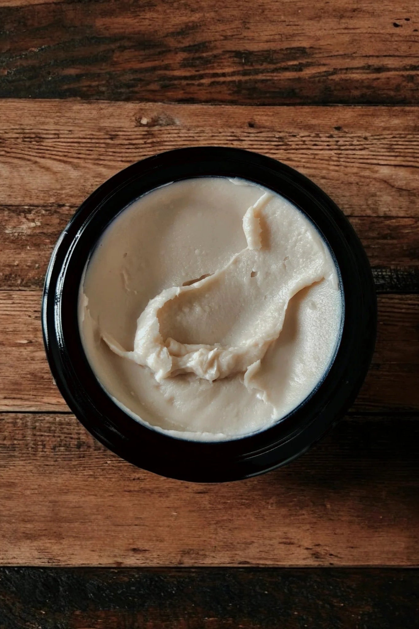 An open jar of 'Rose Remedy' ultra rich face cream by Stay Wild Apothecary is shown on a wooden surface