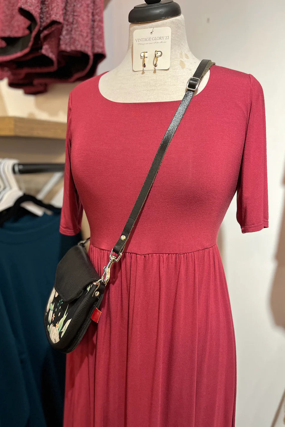 The Doppio Dress by Cherry Bobin in Red with slight scooped neck, half sleeves, a fit and flare shape, and full skirt that falls below the knee, is showon a mannequin in a clothing store.