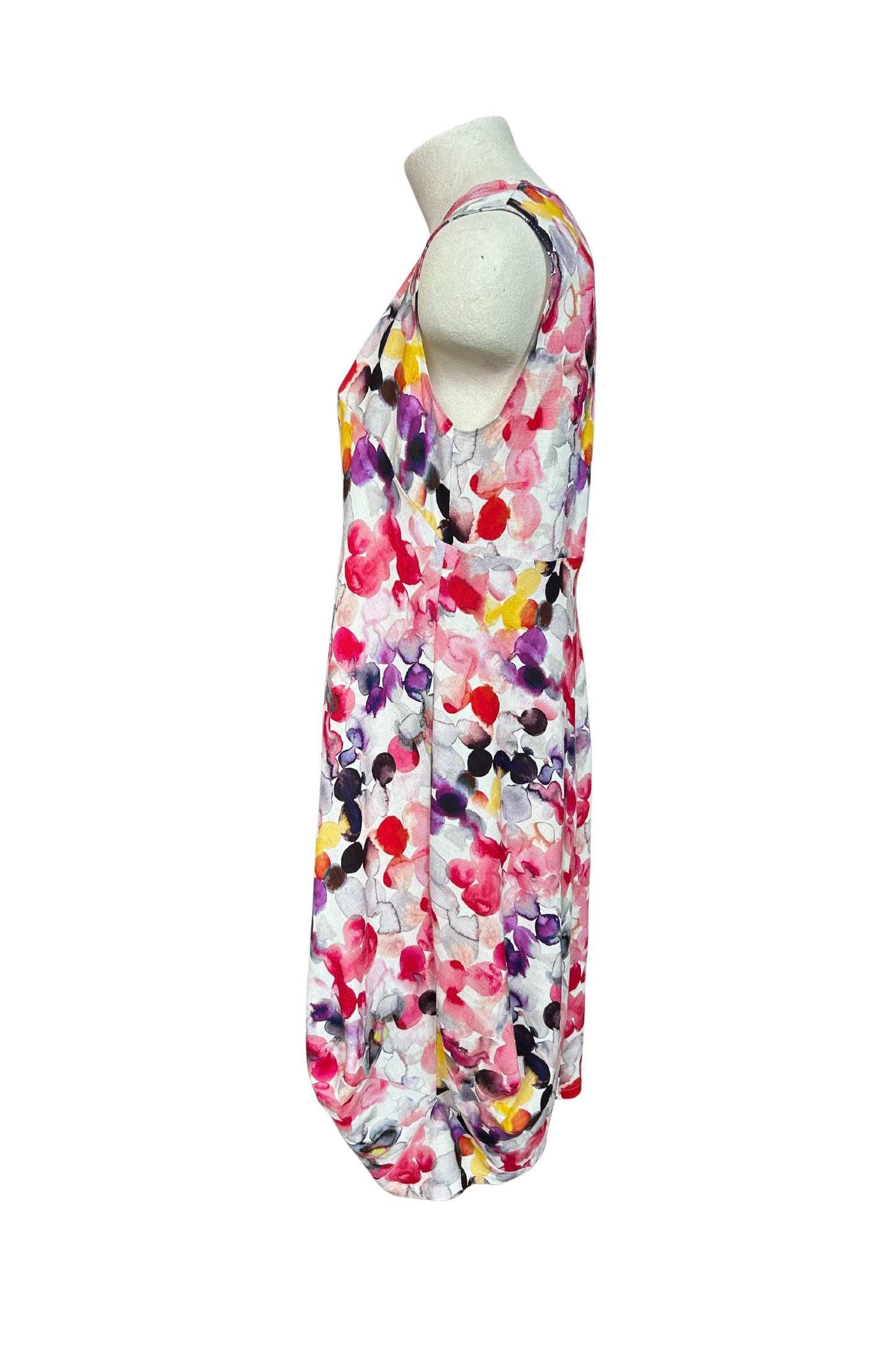 A side view of the Monica Dress by Solomia in Watercolour Print is shown on a mannequin against a white background. It's a sleeveless knee-length dress with a relaxed fit and uniquely angled bottom hem.