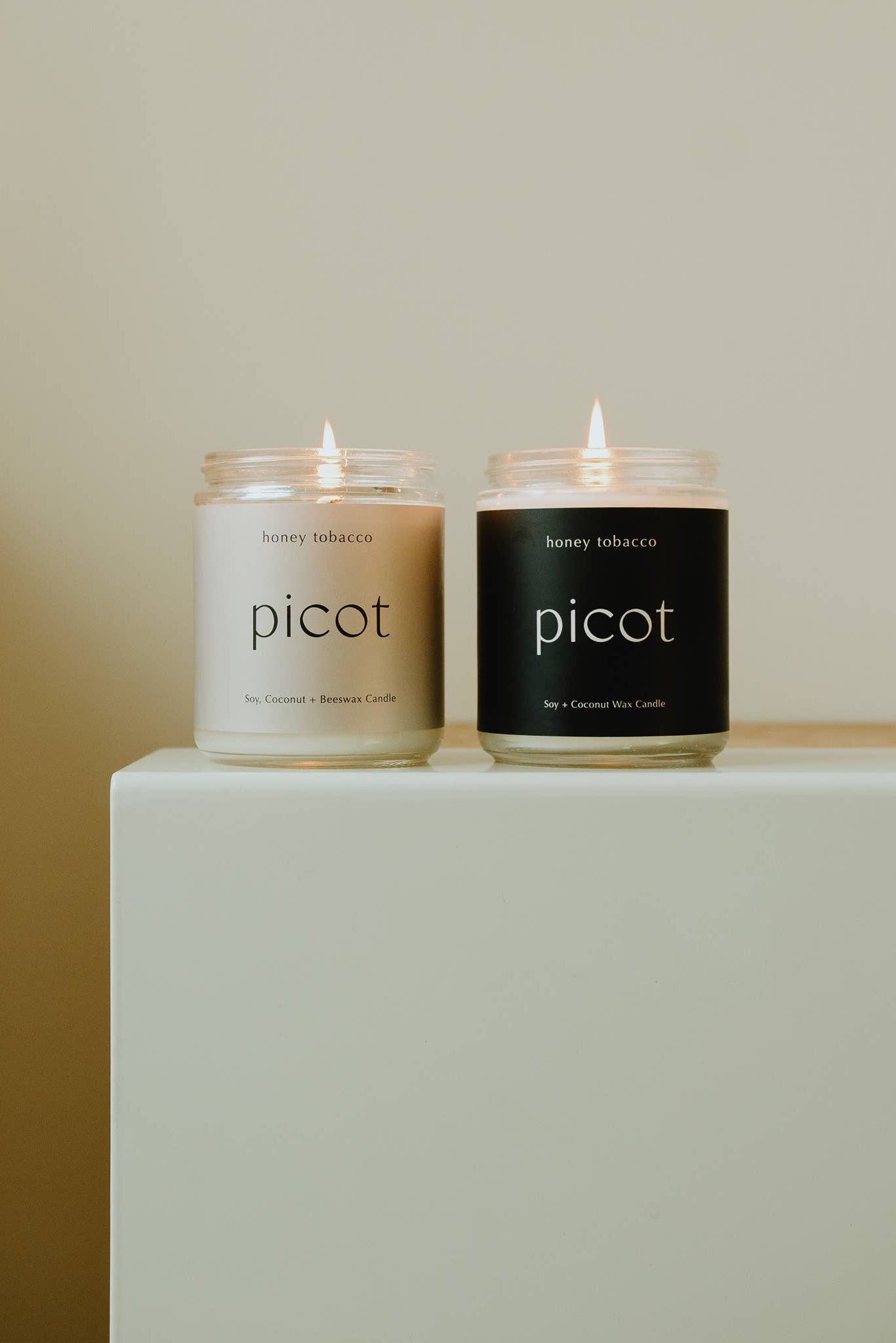 Two Picot candles on a white surface with a beige background