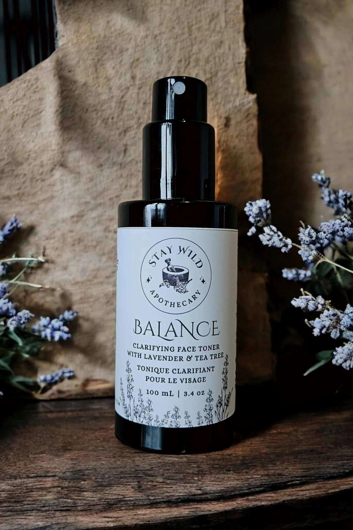 Bottle of 'Balance' face mist by Stay Wild Apothecary shown with lavender flowers on a wooden surface