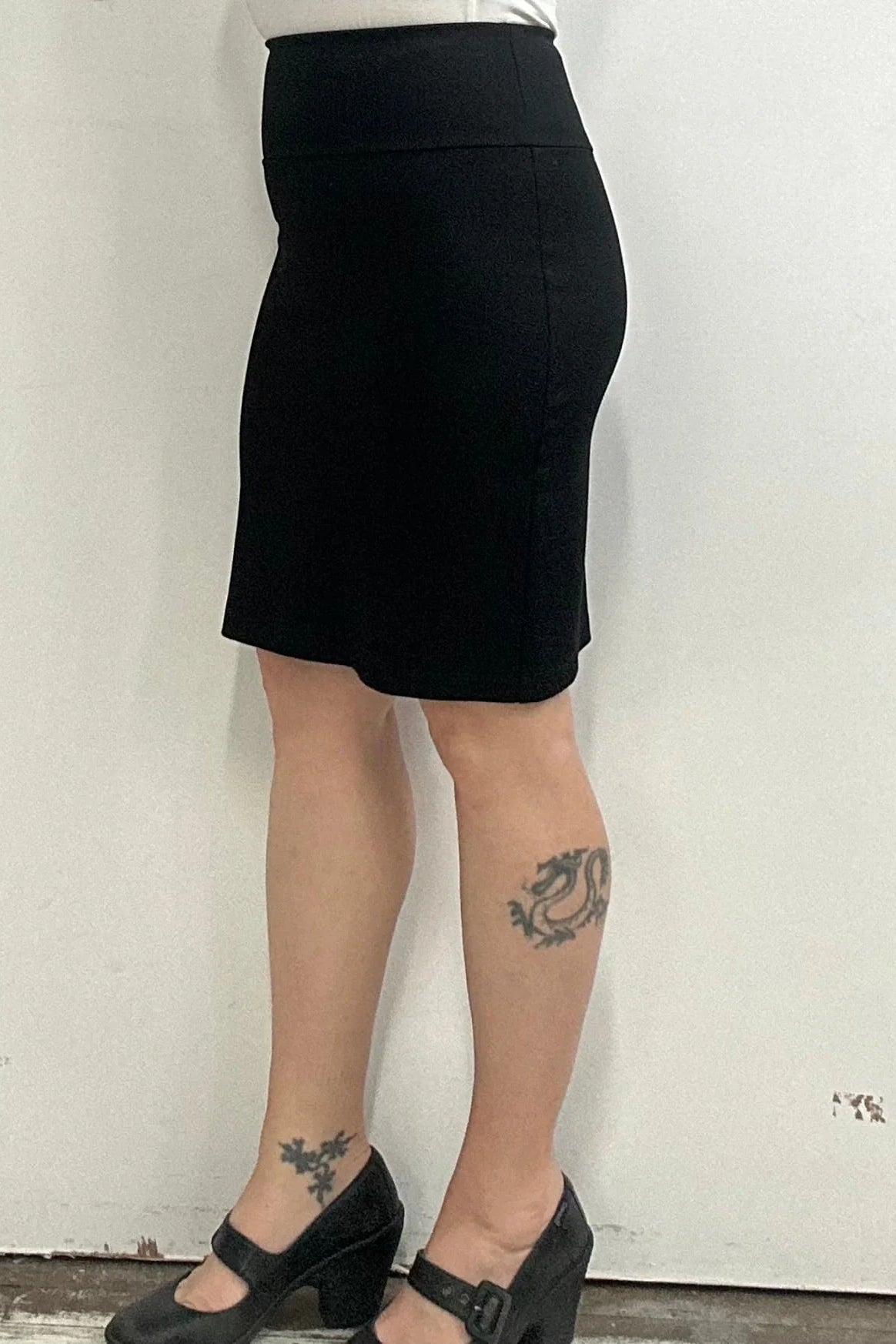 Waist down side view of a woman wearing the Veneto Skirt by Kollontai in Black, a pencil skirt with a wide-pull on waistband that hits above the knee.