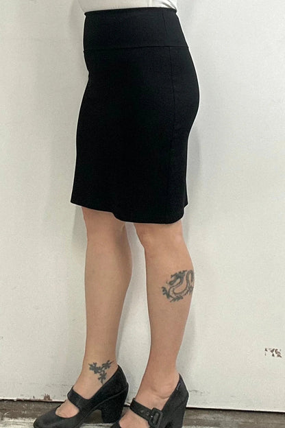 Waist down side view of a woman wearing the Veneto Skirt by Kollontai in Black, a pencil skirt with a wide-pull on waistband that hits above the knee.