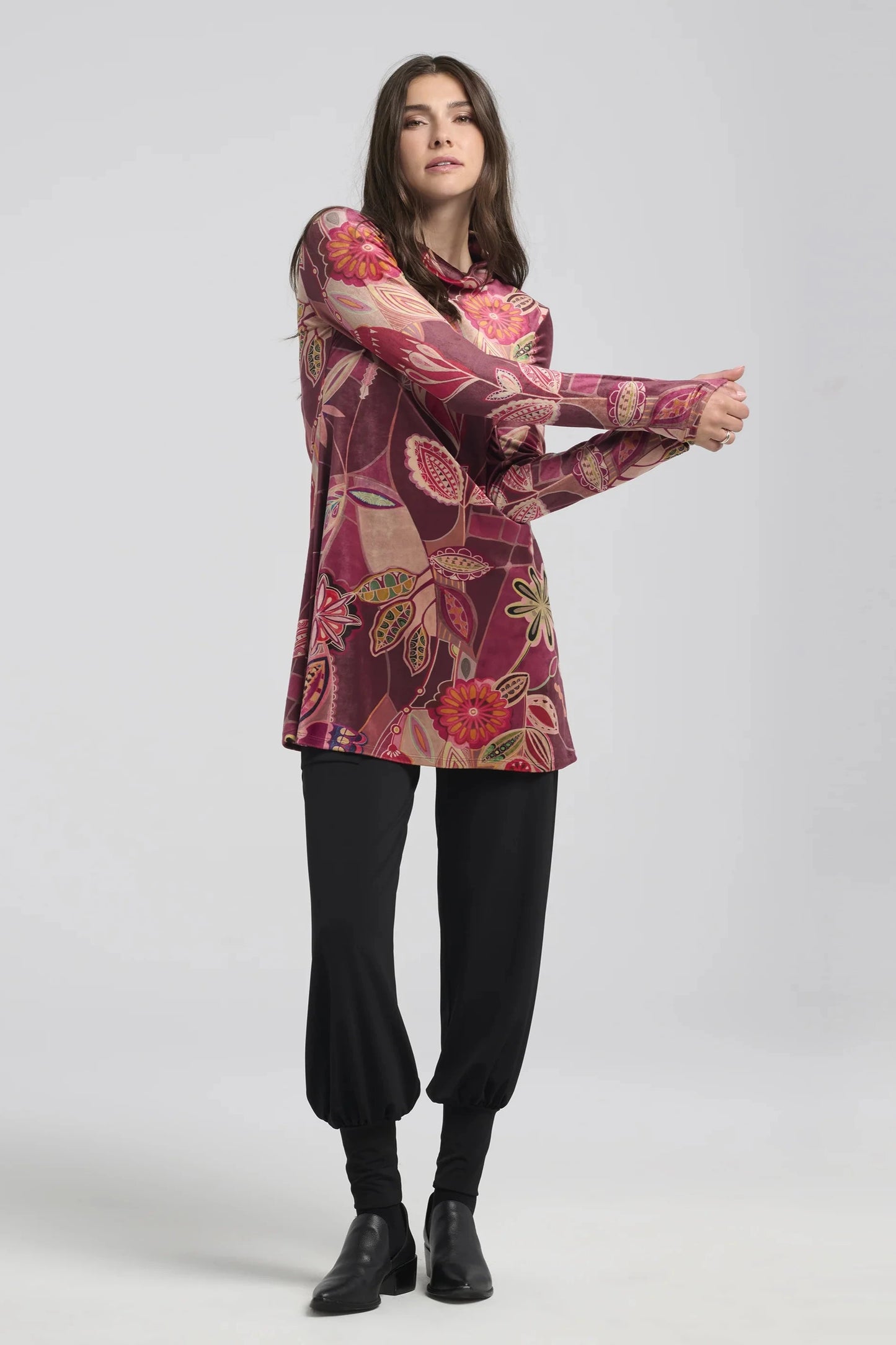 A woman wearing the Holly Tunic by Kollontai, with a Purple print, high neck, long sleeves and A-line shape, with black pants.