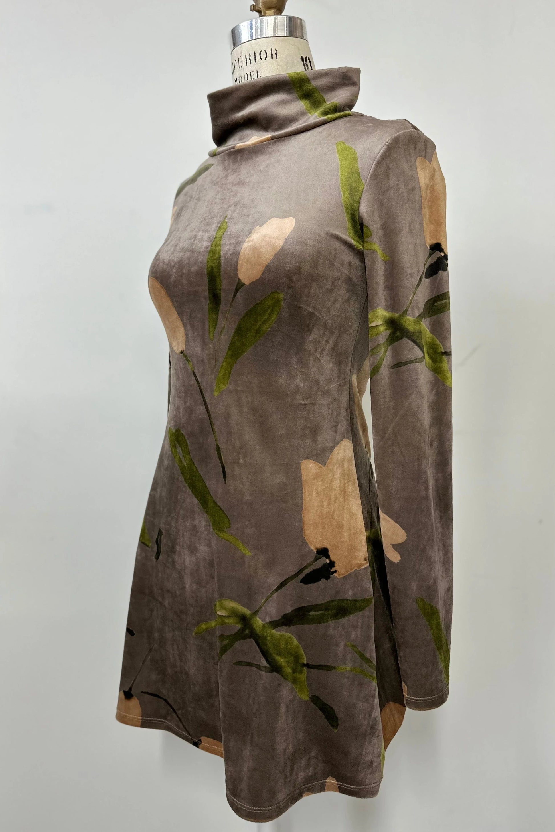 The Holly Tunic by Kollontai in Taupe, an Italian velvet A-line tunic with a turtleneck, long sleeves, and a floral print, is shown on a mannequin against a  a grey background. 
