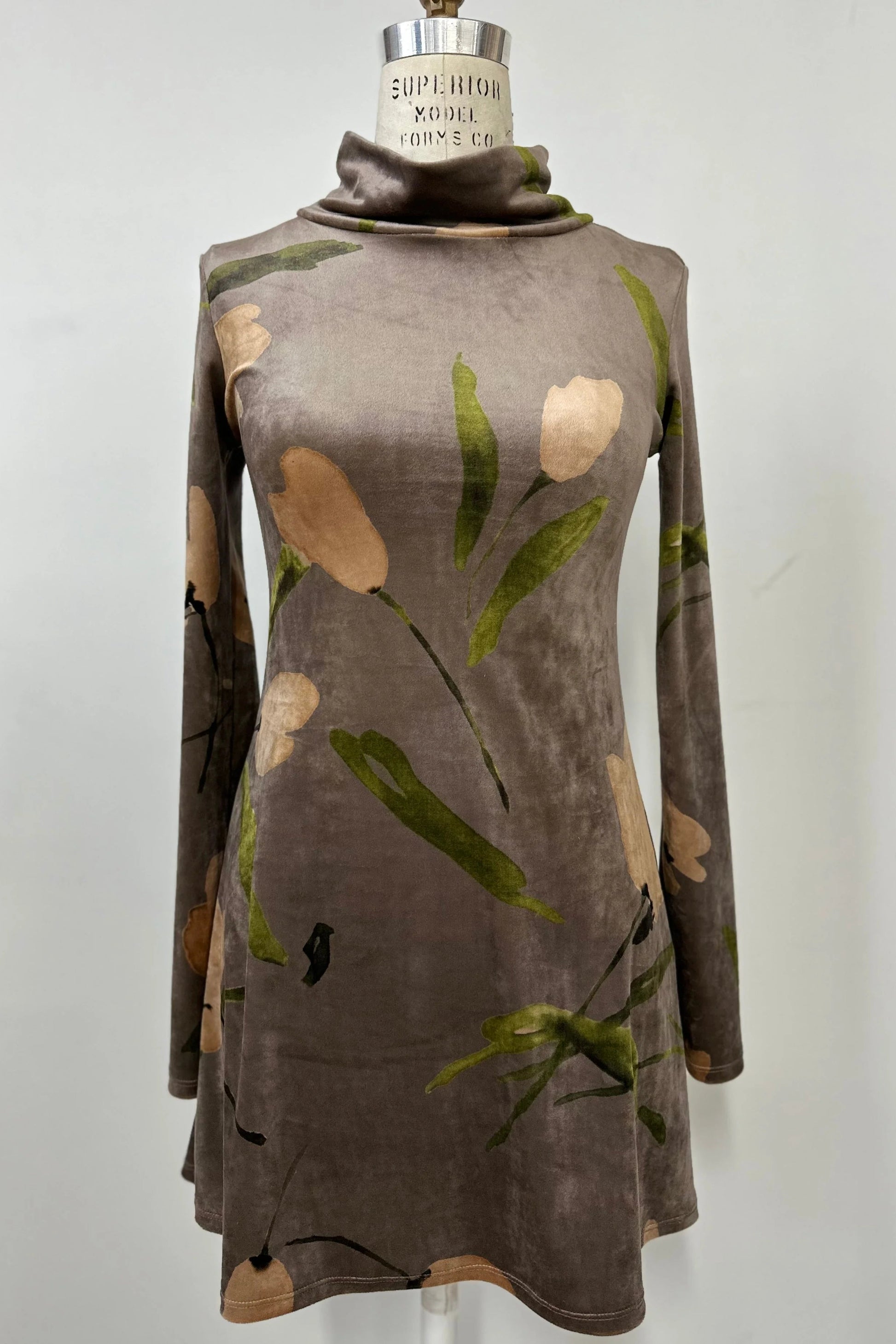 The Holly Tunic by Kollontai in Taupe, an Italian velvet A-line tunic with a turtleneck, long sleeves, and a floral print, is shown on a mannequin against a  a grey background. 