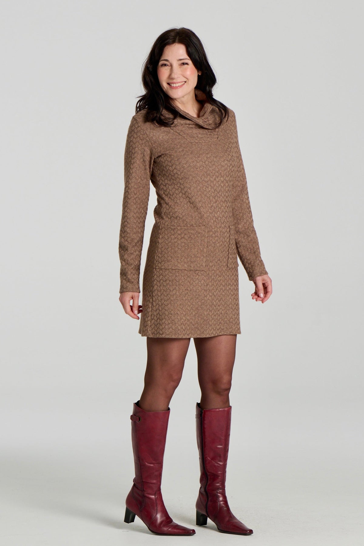 A woman wearing the Sacha Tunic by Kollontai in Brown, a textured knit straight cut tunic with a funnel collar and large patch pockets. She is standing in front fo a white background. 