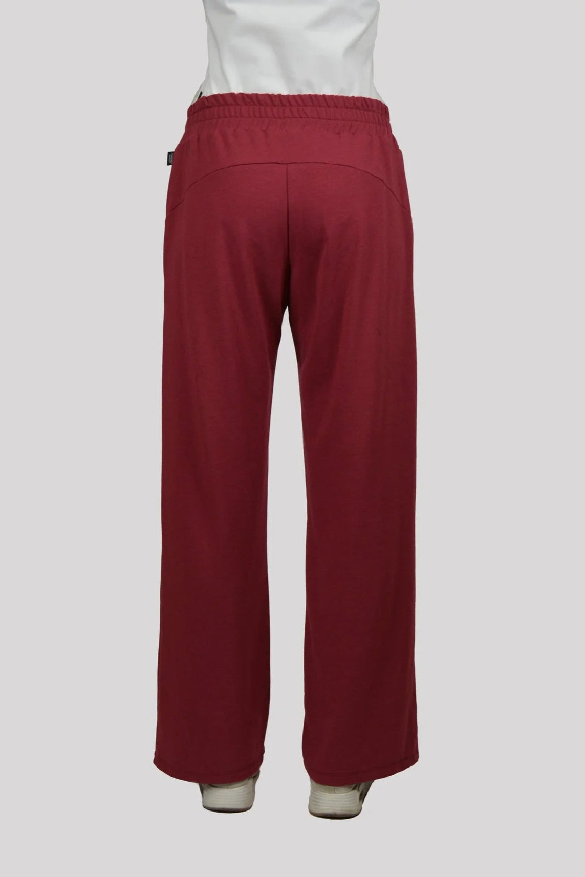 Back waist down view of the Tadoussac Pants by Message Factory in Raspberry: flared sweatpants with an elastic waist in a bamboo/cotton blend. She is wearing a white tank with them and is standing in front of a white background. 