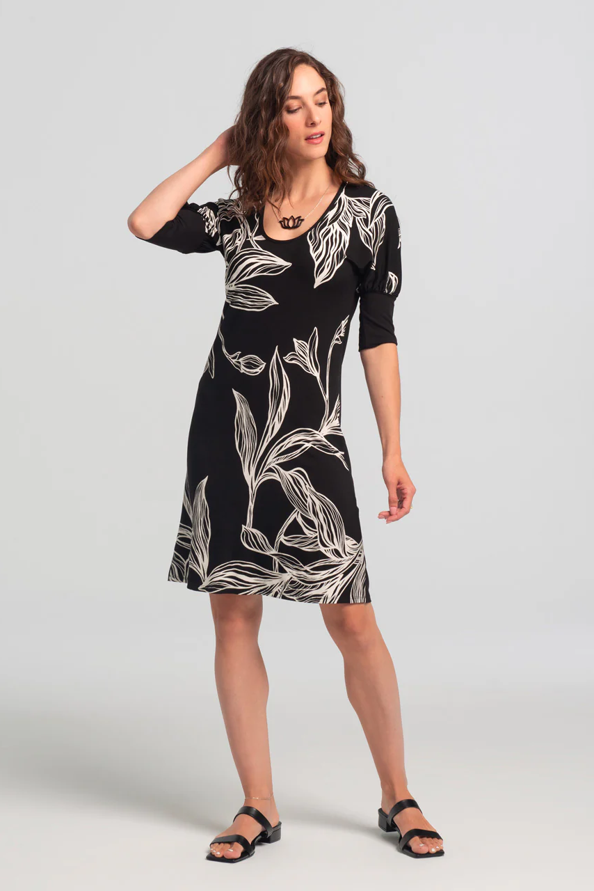 Woman wearing the Jaya Dress by Kollontai, featuring a black and white leaf print, standing in front of a white background 