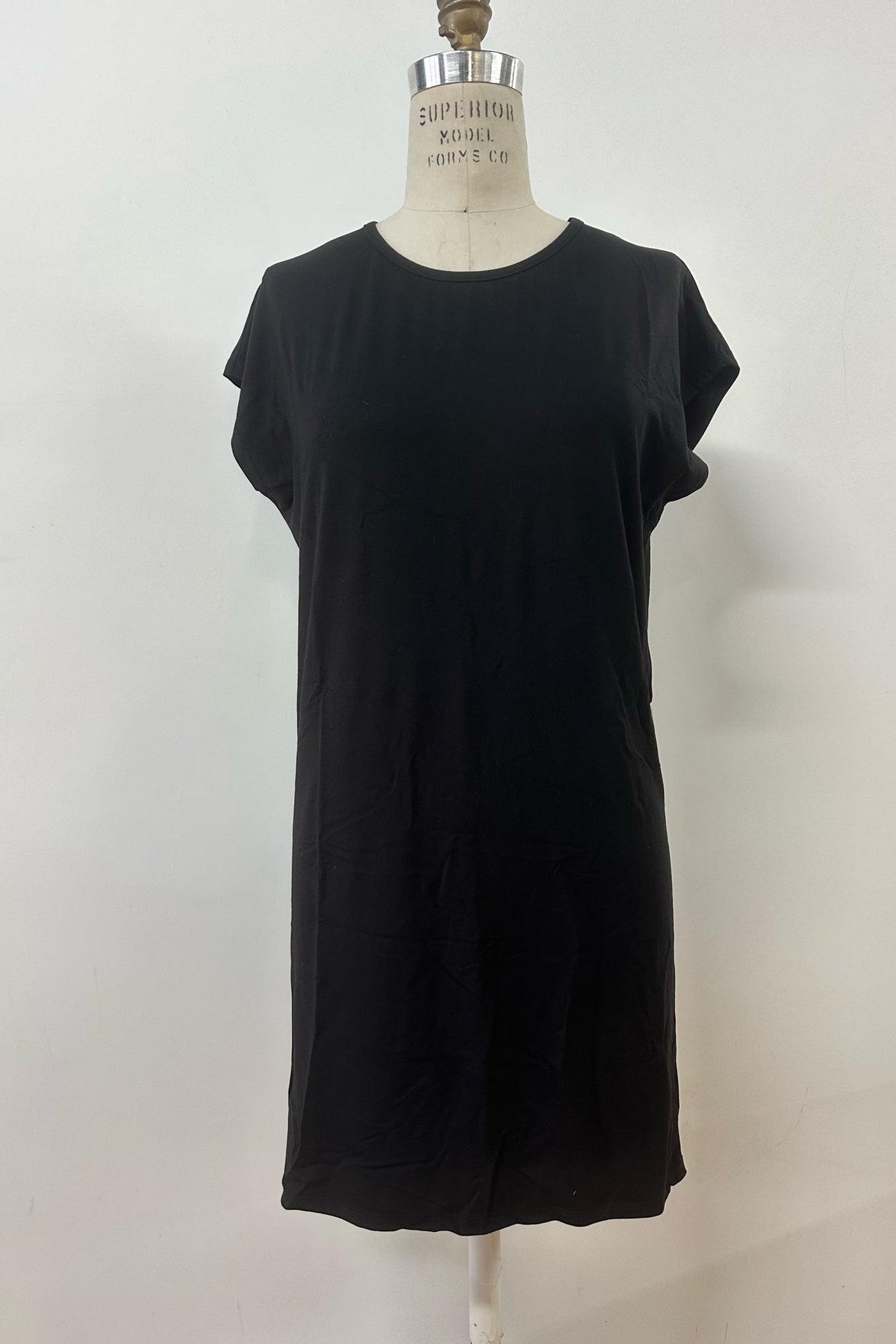 The Arwen Dress by Kollontai, a Black t-shirt dress with a round neck, short extended sleeves, a loose ft, and an above the knee hem, is shown on a mannequin in front of white background. 