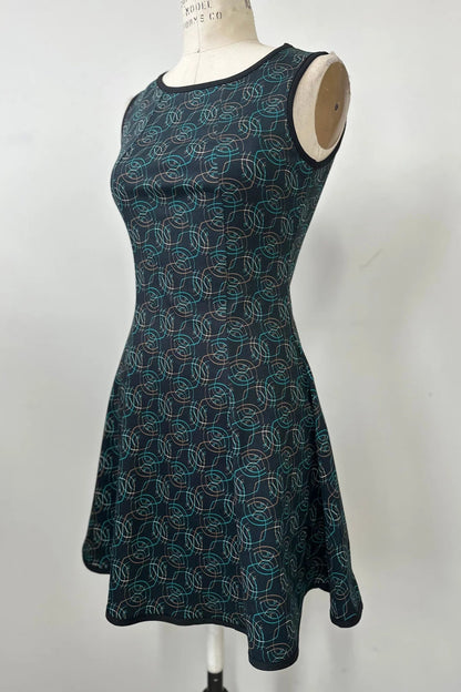 The Silba Dress by Kollontai in a Turquoise on black print, a sleeveless dress with a round neck, fit and flare shape, and above the knee hem, is shown on a mannequin against a white background. 