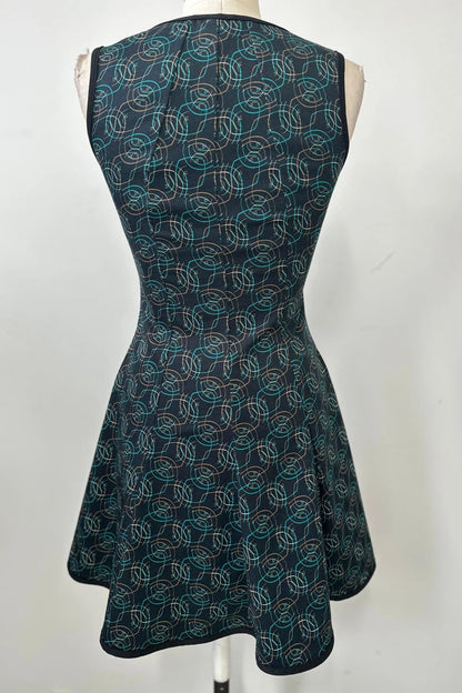 A back view of the Silba Dress by Kollontai in a Turquoise on black print, a sleeveless dress with a round neck, fit and flare shape, and above the knee hem, is shown on a mannequin against a white background. 