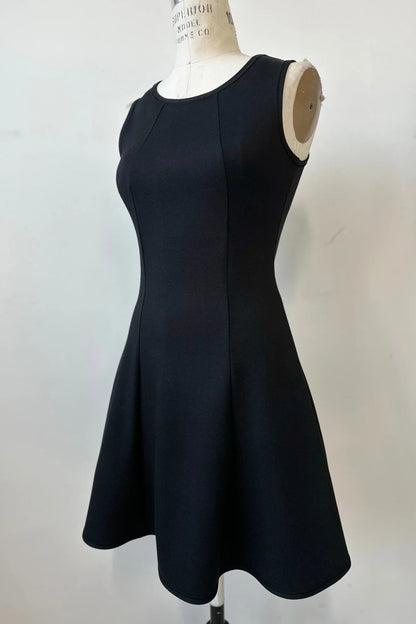 The Toscana Dress by Kollontai in Black, a sleeveless piece with a round neck, princess seams, and fit and flare shape with a full skirt that hits above the knee, is shown on a mannequin against a white background. 
