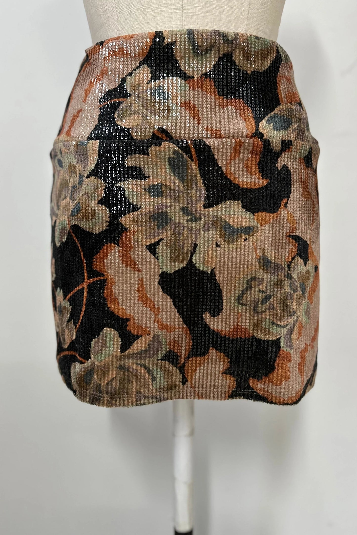The Soleste Skirt by Kollontai, a floral velvet miniskirt in autumn tones with clear sequins sewn right into the fabric and a wide pull-on waistband, is show on a mannequin in front of a white background. 