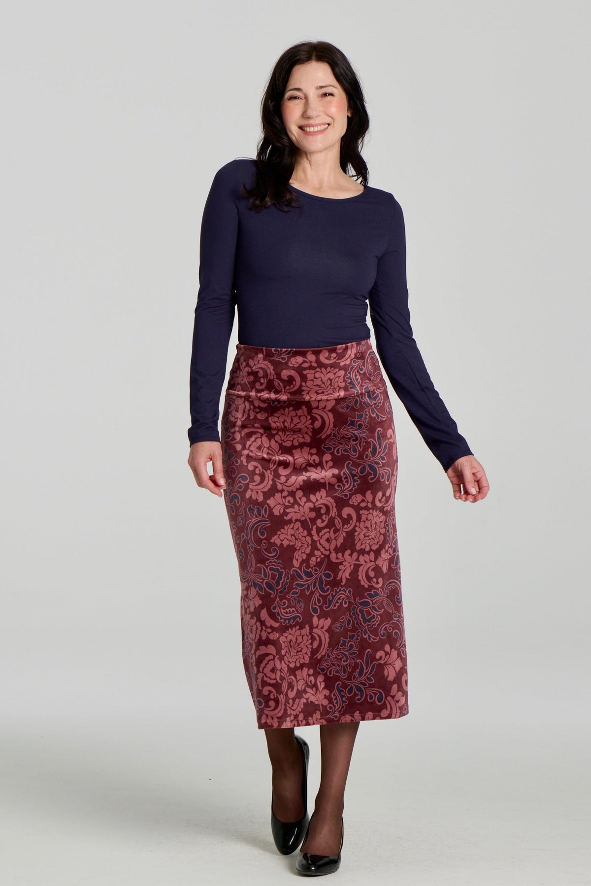 A woman wearing the Loretto Top by Kollontai in Navy, a slim fitting long sleeved top with a round neck. She is wearing it with the Winslet Skirt and standing in front of a grey background. 