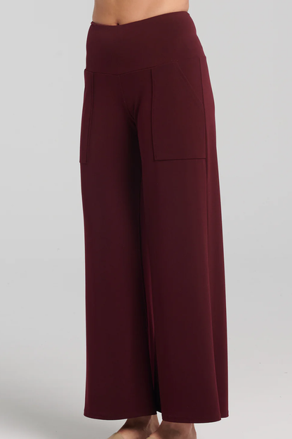 Waist-down side-view photo of woman wearing the Ramy Pants by Kollontai in Plum, standing in front of a white background 