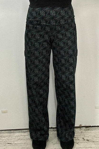 Waist down view of a woman wearing the Elma Pants by Kollontai in Turquoise on black print, straight legged pants with a wide elastic waist and large slant pockets. 
