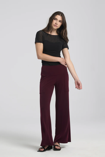 Photo of a woman wearing the Ramy Pants by Kollontai in Plum with a black t-shirt, standing in front of a white background 