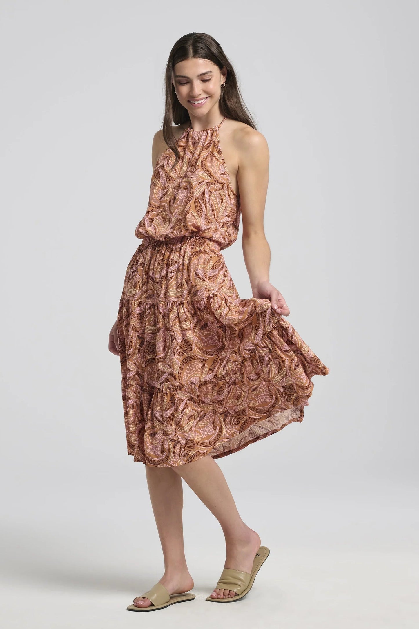 A woman wearing the Semira Camisole by Kollontai in Cinnamon print, a lightweight top with an adjustable halter neck and a loose fit. She is wearing it with a matching skirt  and is standing in front of a white background. 