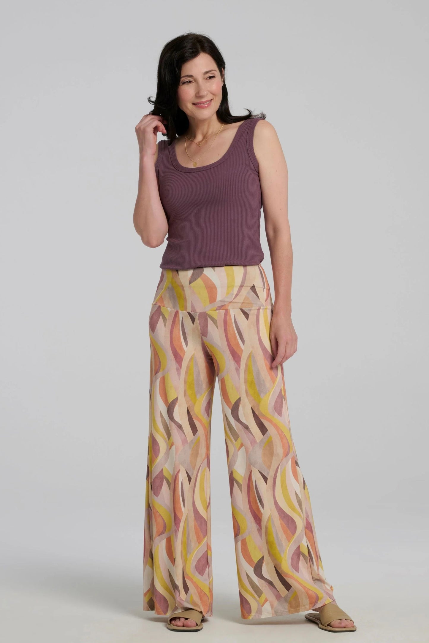 A woman wearing the Rina Camisole from Kollontai, a ribbed tank in stretchy bamboo with side straps and a scooped neck front and back.  She is wearing it with the Sorela Pants and standing in front of a white background. 