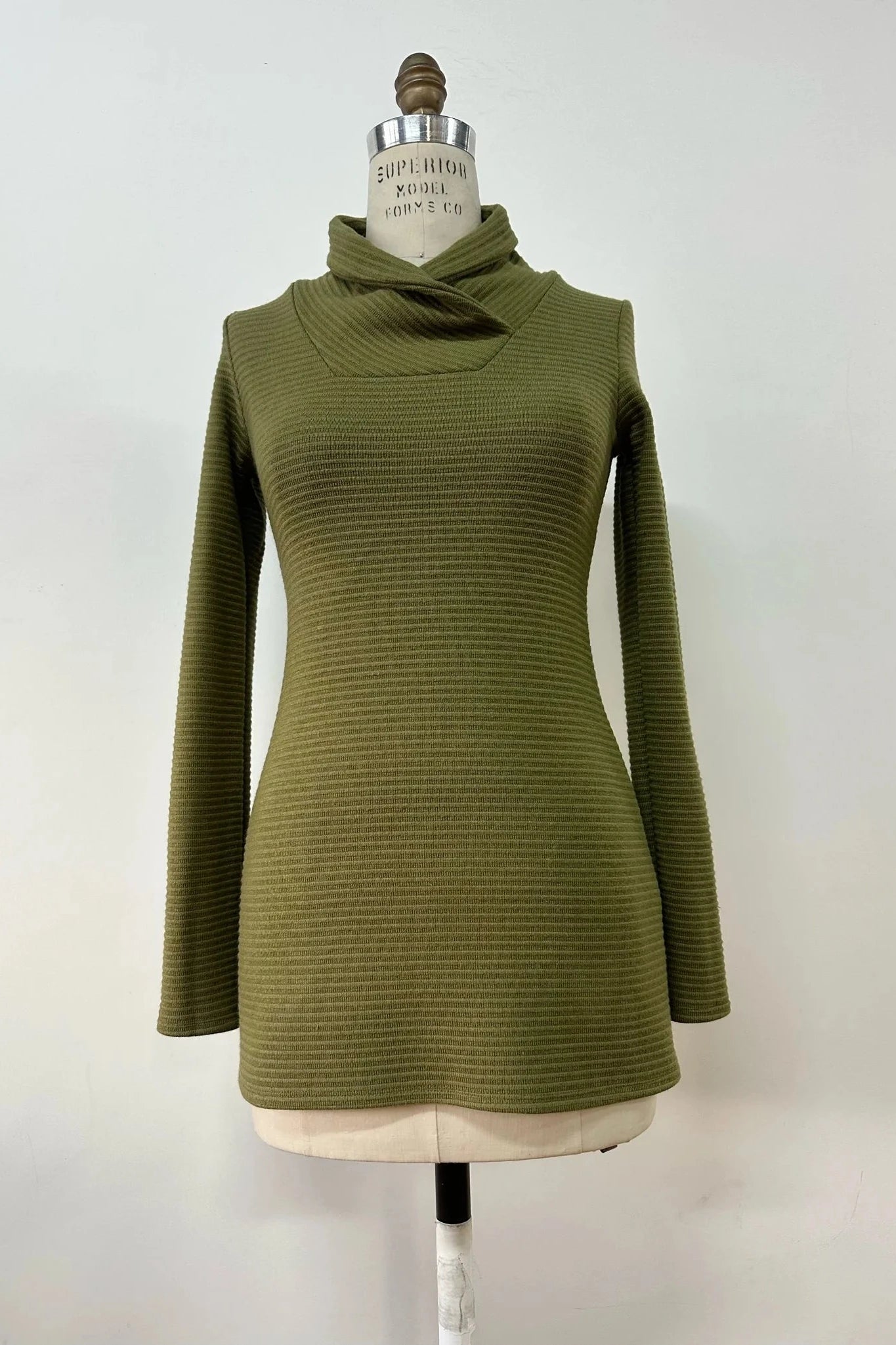 The Beaufort Sweater by Kollontai in Green, featuring a cross-over cowl neck, long sleeves and a ribbed knit, is show on a mannequin.