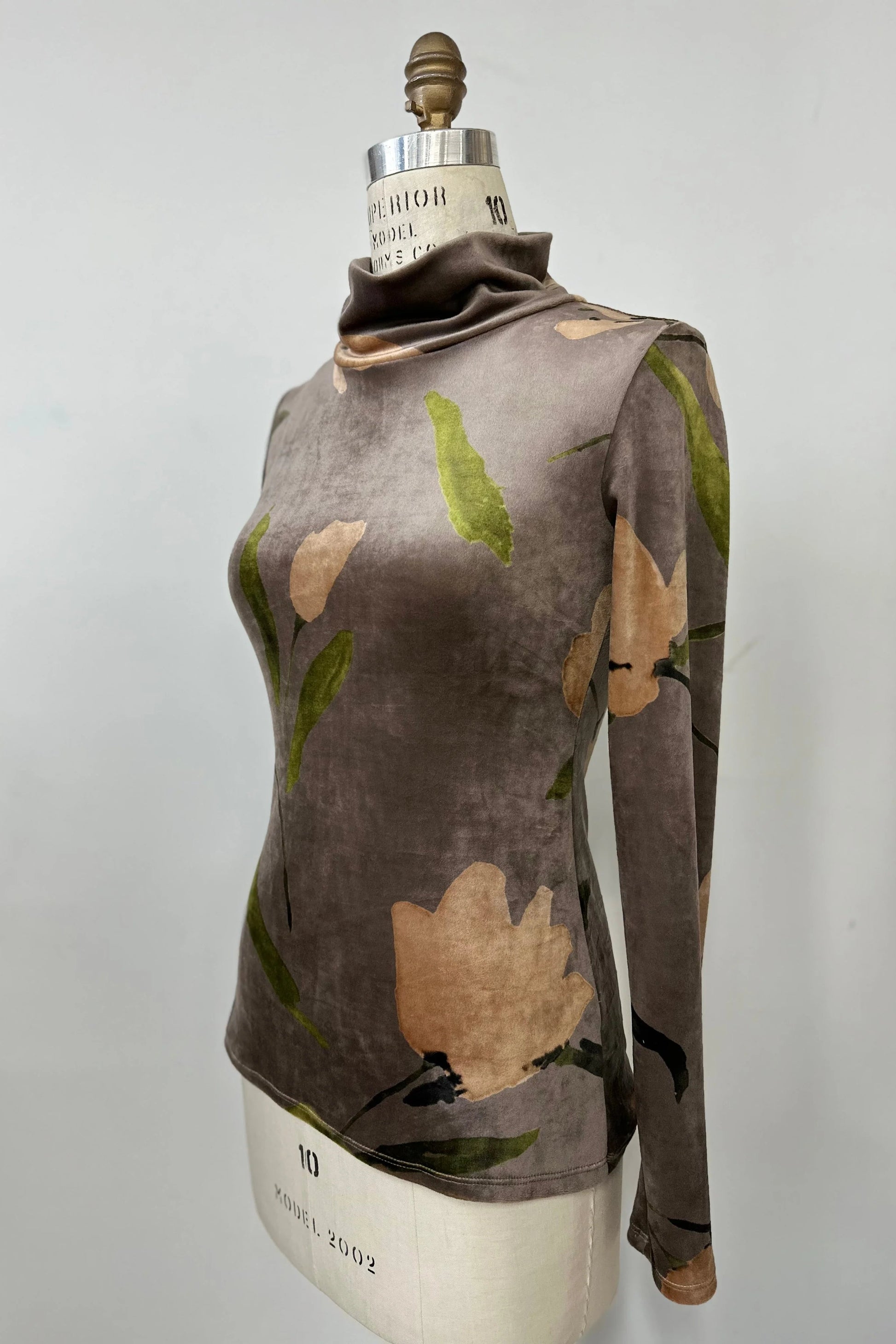 The Everdeen Turtleneck by Kollontai in Taupe, a velvet top with a floral print, is shown on a mannequin in front of a grey background. 