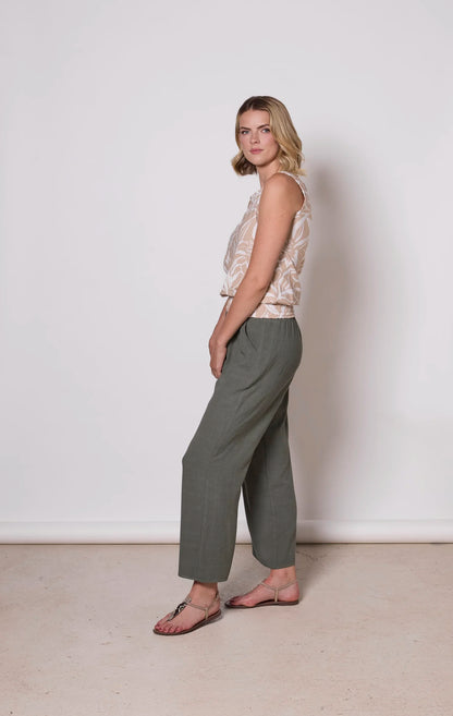 Side view of a woman wearing the Heidi Pants by Tangente in Thyme, wide legged slightly cropped pants with an elastic waist. She is wearing them with a printed beige tank top and standing in front of a white background. 