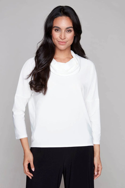 A woman wearing the Perry Top by Compli K in Ivory, featuring a cowl neck, 3/4 drop sleeves, and decorative buttons up the back. She is wearing it with black pants and standing in front of a white background. 