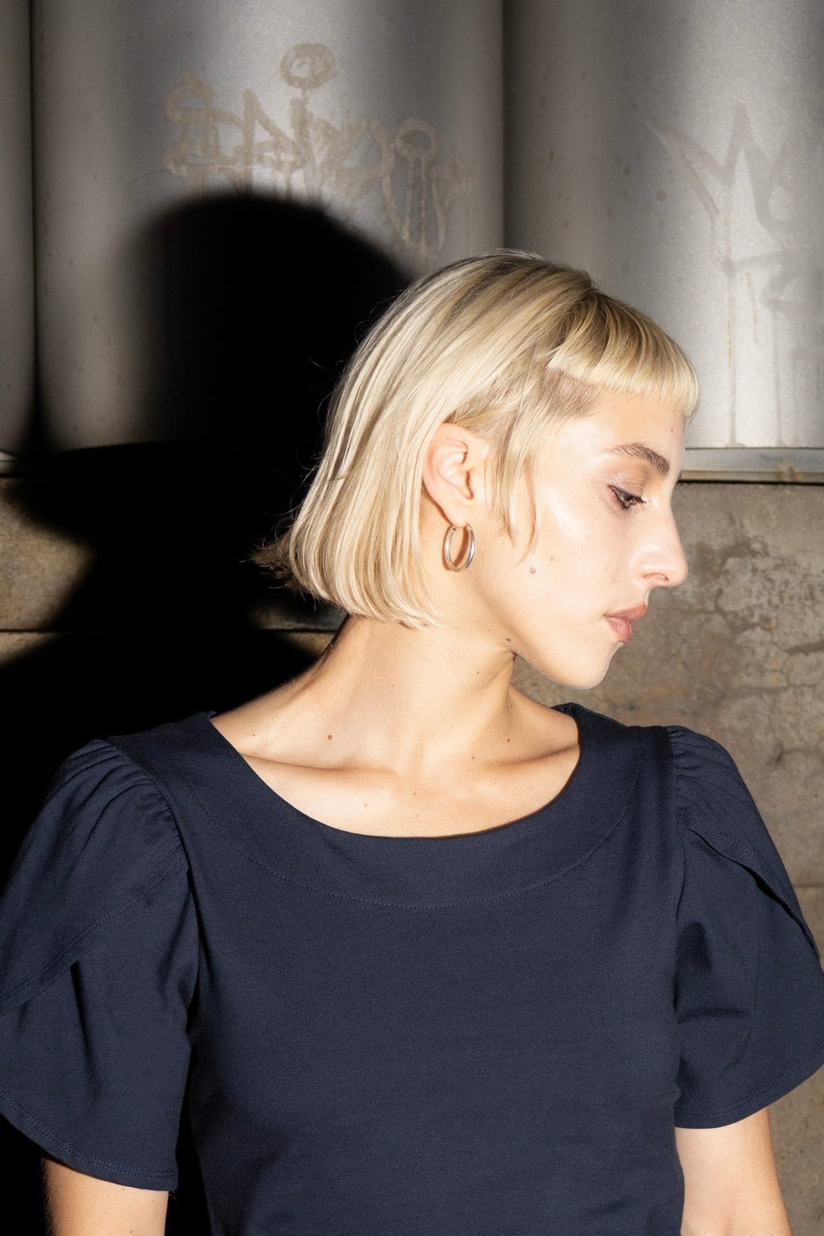 Close up view of a woman wearing the Opal Dress by Eve Lavoie in Navy, a short dress with tulip sleeves, and an A-line shape. She's standing outdoors by metal and concrete. 