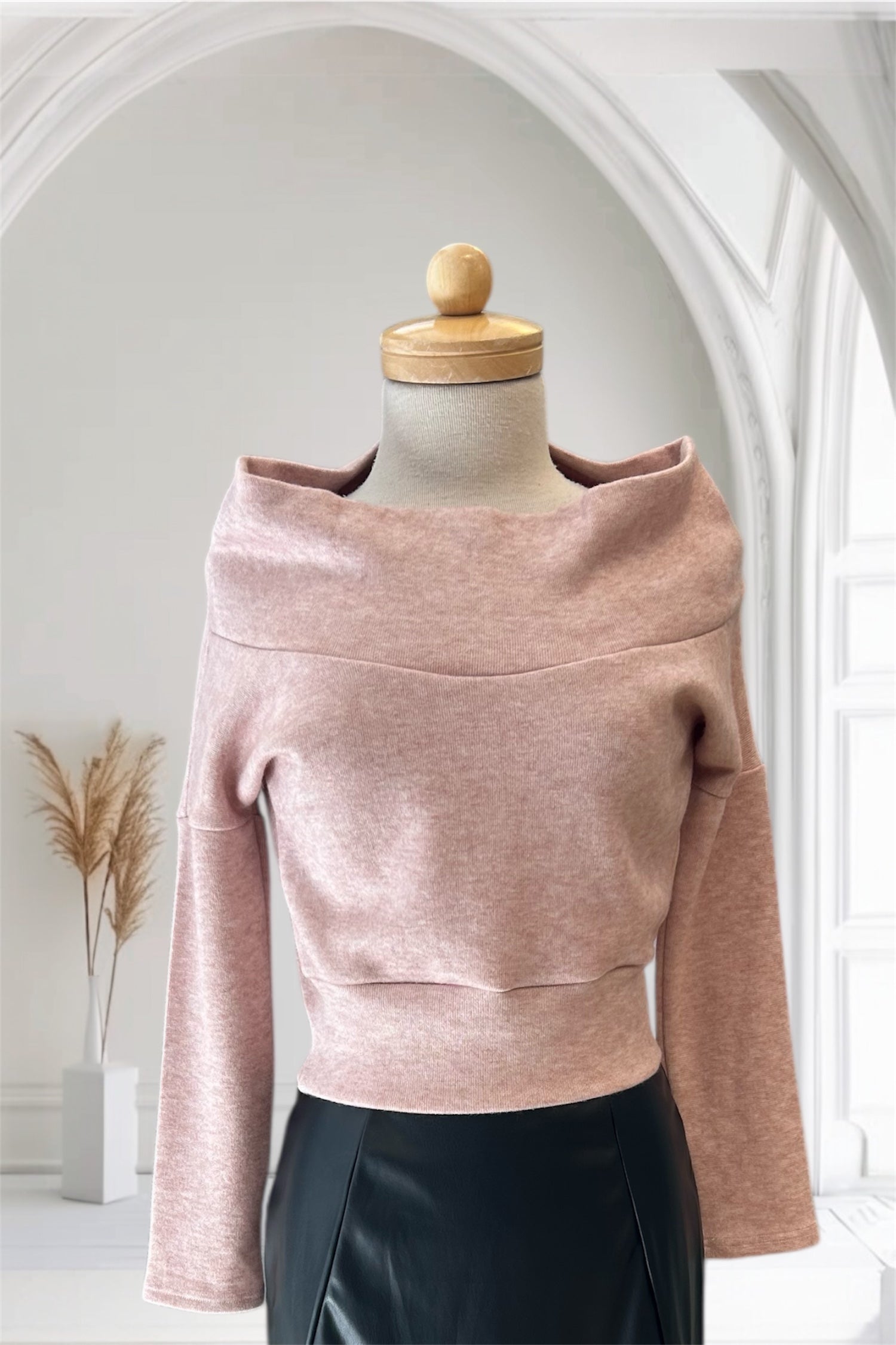The Changes Sweater by Allison Wonderland in Pink, featuring a large cowl neck, long dropped sleeves, and a wide waistband, is shown with the Desire Skirt in Black against a white arched backdrop. 