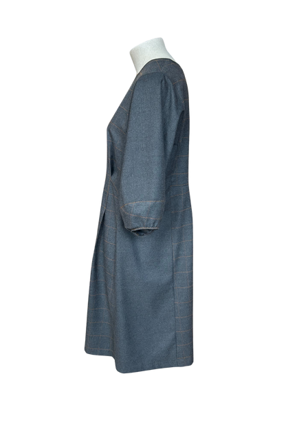 A side view of the Hanna Dress by Solomia in Grey is shown on a mannequin against a white background. This knee length dress has uniquely placed pleats and seams to create an architectural shape, with 3/4 length sleeves with structured cuffs. It has checked fabric on the front, back and cuffs, and solid grey fabric at the sides. 
