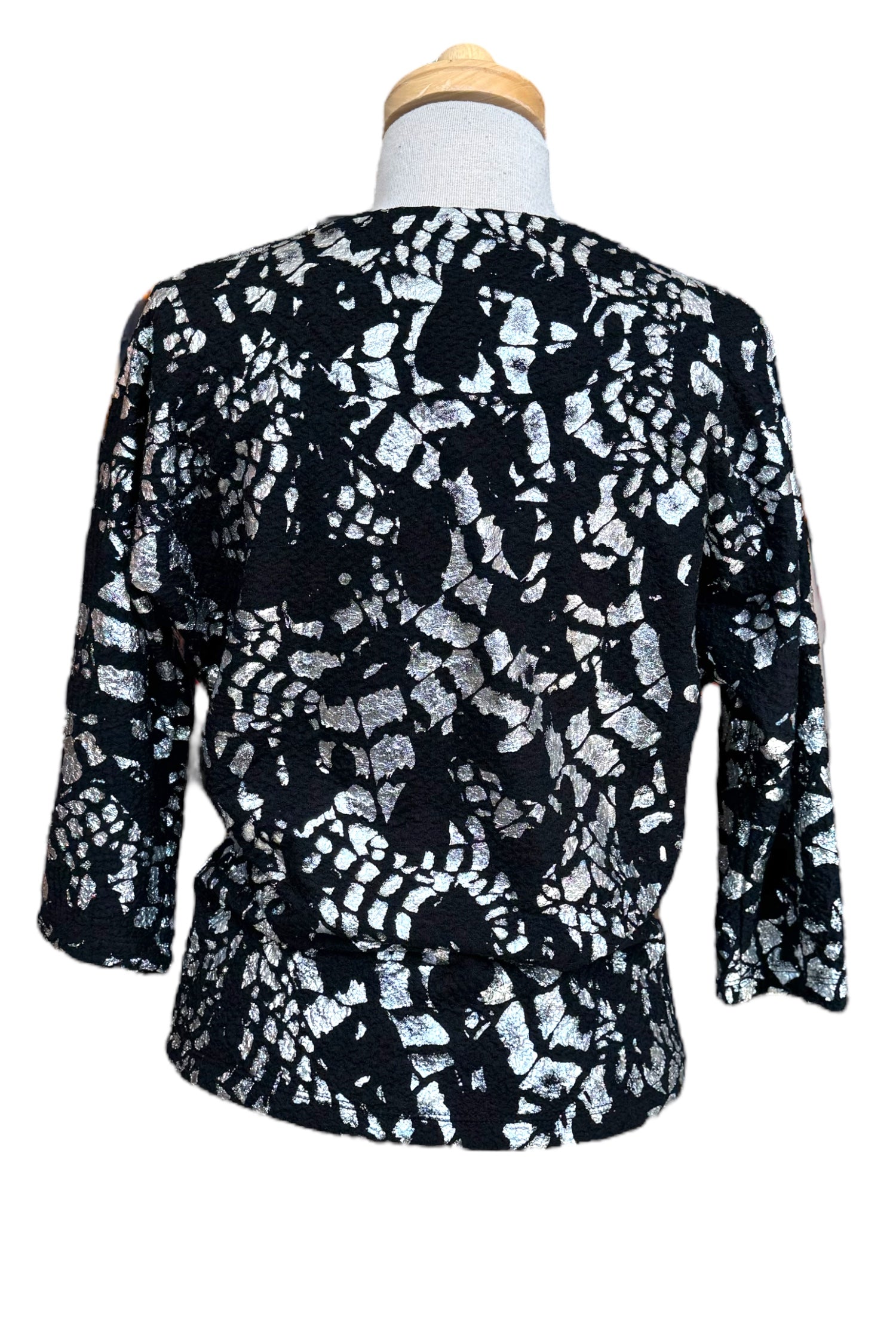 A back view of the Posey Sweater from Compli K in Black and Silver, with a round neck, 3/4 sleeves, and a tie detail at the waist, with black pants, is shown on a mannequin in front of a white background. 