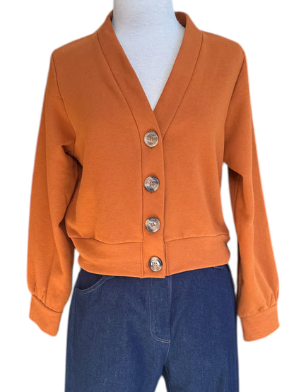 The Douglas Fleece Cardigan by Eve Lavoie in Pumpkin, a short cardigan with tortoiseshell buttons and a wide waistband, is shown with jeans on a mannequin against a white background