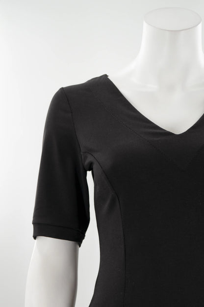 A detail of the FW Classic Dress by Karkass in Black, with short sleeves, a v-neck, and fit and flare shape that falls to the knee, is shown on a mannequin against a white background