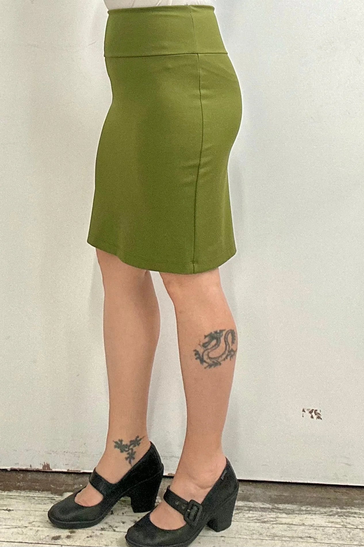 Waist down side view of a woman wearing the Veneto Skirt by Kollontai in Granny Smith, a pencil skirt with a wide-pull on waistband that hits above the knee.