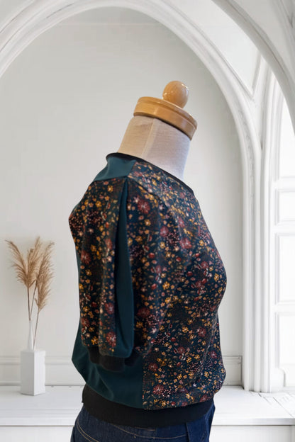 A side view of the Darling T-Shirt by Slak in Floral with Green, a short sleeved, semi-fitted sweater with contrasting fabric at the cuffs, collar and hem, inserts on the sleeves, and a solid back, is shown on a mannequin against a white background. 