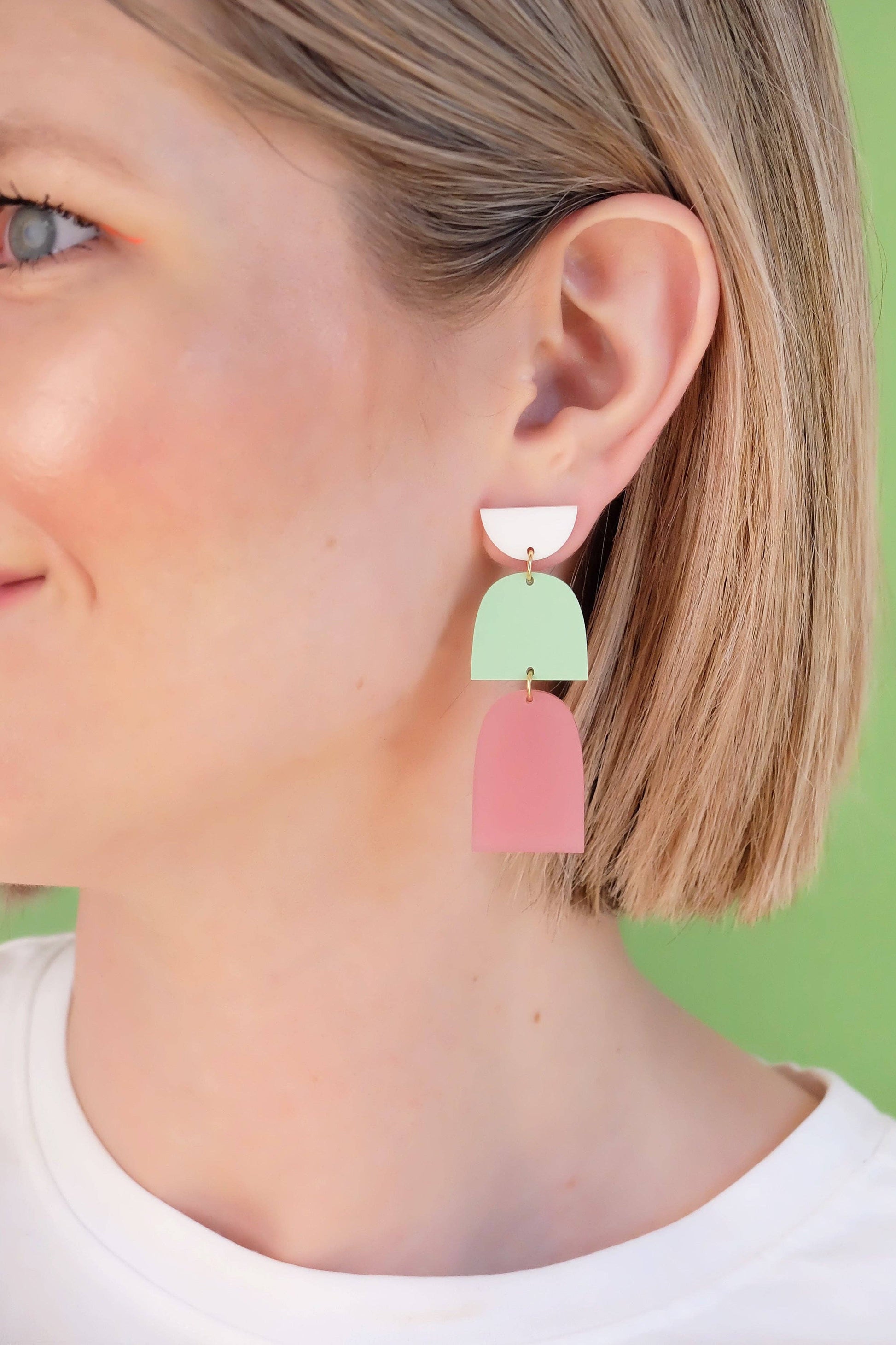 Close-up of a person wearing colorful earrings against a green background