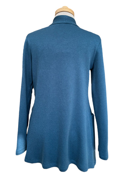 A back view of the Penny Cardigan by Compli K in Peacock, a long open knit cardigan with long sleeves and large patch pockets, is shown on a mannequin against a white background.