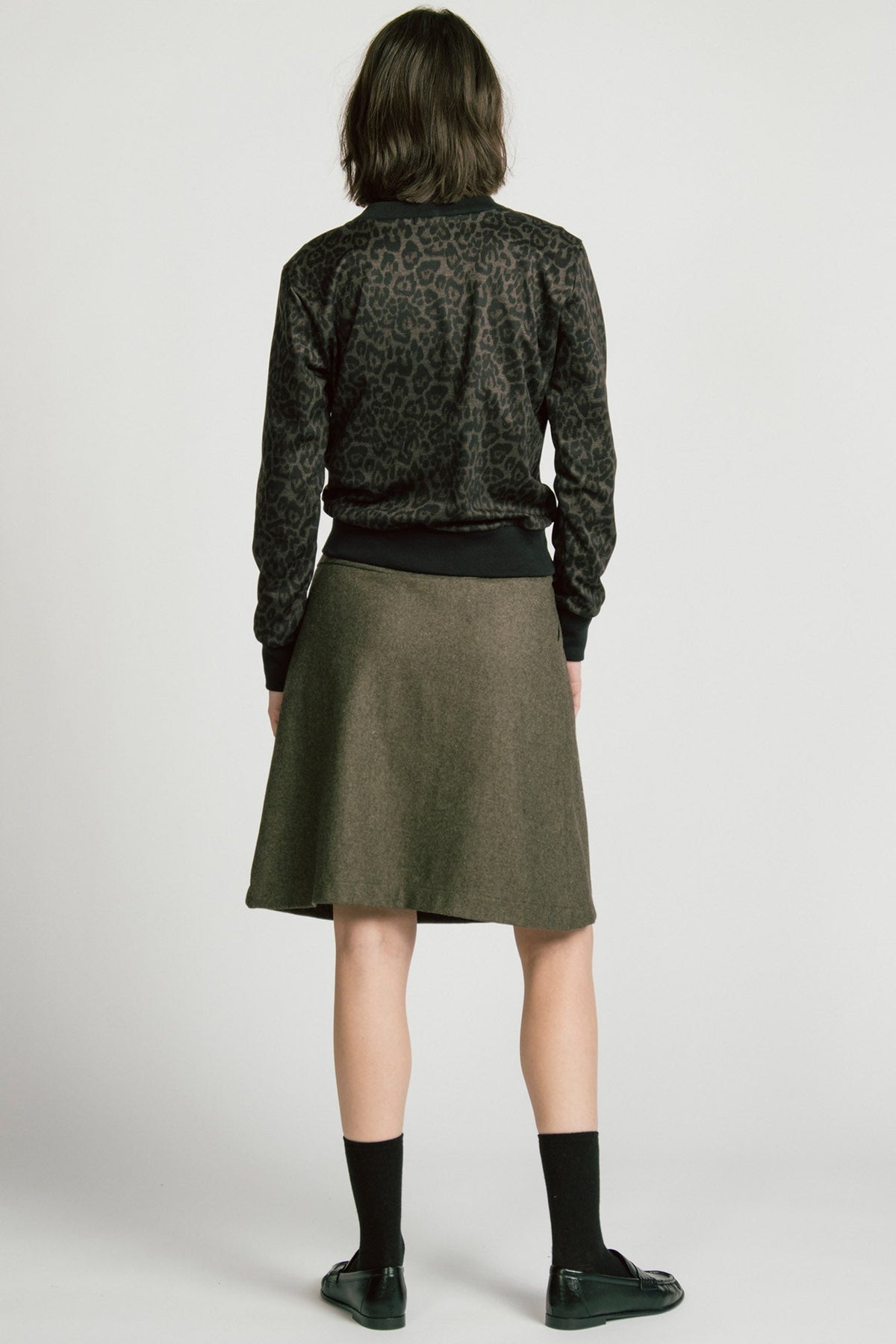 Back view of a woman wearing the Crux Sweatshirt by Allison Wonderland in Animal Print. she is wearing it with a grey skirt and standing in front of a white background. 