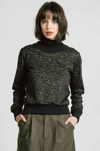 A woman wearing the Crux Sweatshirt by Allison Wonderland in Animal Print. she is wearing it with a grey skirt and standing in front of a white background. 