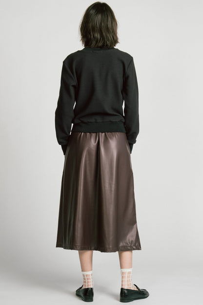 Back view of a woman wearing the Crux Sweatshirt by Allison Wonderland in Black Texture. she is wearing it with a brown pleather skirt and standing in front of a white background. 