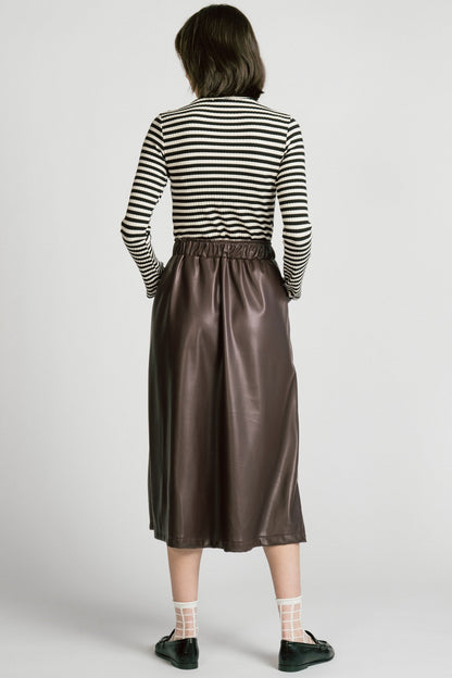 Back view of a woman wearing the Octans Turtleneck by Allison Wonderland in black and white Stripe, a ribbed turtleneck. She is wearing it with a brown pleather skirt and standing against a white studio background.