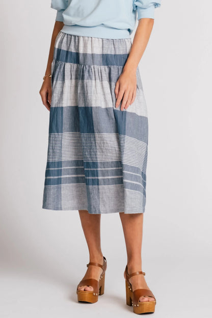 Waist down view of a woman wearing the Pelican skirt by Allison Wonderland in Blue Plaid, a mid-calf length tiered skirt with an elastic waist. She is wearing it with the Finch Sweatshirt in Baby Blue and standing in front of a plain background. 