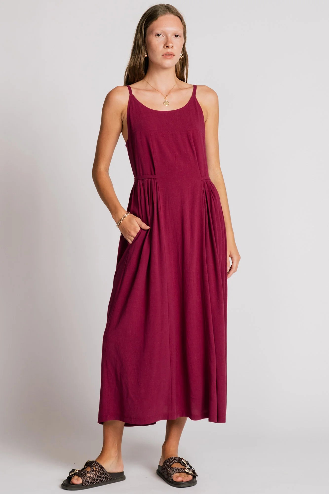 A woman wearing the Swan Dress by Allison Wonderland in Pink, a maxi dress with spaghetti straps, and ties at the waist. 