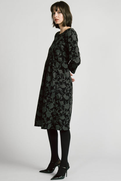 Side view of a woman wearing the Virgo Dress by Allison Wonderland in Floral, a babydoll style dress in floral printed fine wale corduroy with bracelet length sleeves and a midi length. She's standing against a white background. 