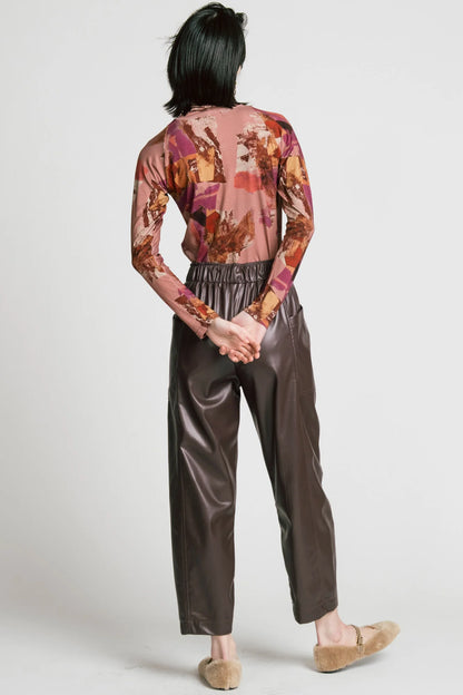 Back view of a woman wearing the Aches Turtleneck by Allison Wonderland in Burgundy print, a slim fitting classic turtleneck in an abstract pattern. She is wearing it with brown faux leather pants and standing in front of a white background. 