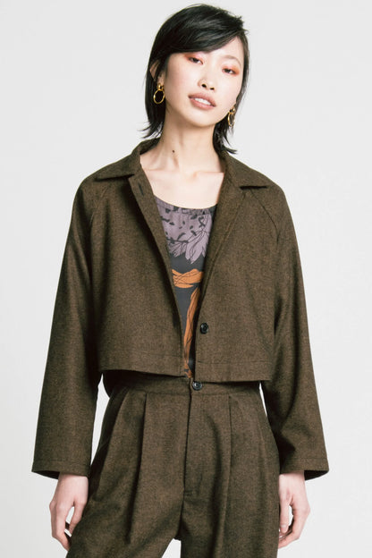 3/4 view of a woman wearing the Cycle Jacket by Allison Wonderland in brown Herringbone, a cropped jacket with a lapel collar, button front, and raglan sleeves. She is wearing it with the Flash top in Horse print and the matching Memory Pants and standing in front of a white background. 