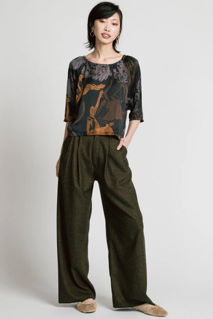 A woman wearing the Flash Blouse by Allison Wonderland in Horse Print, featuring 3/4 dropped raglan sleeves, a boat neck with gathers at the shoulders, and a loose fit. She is wearing it with the Memory Pant in Herringbone and standing in front of a white background. 